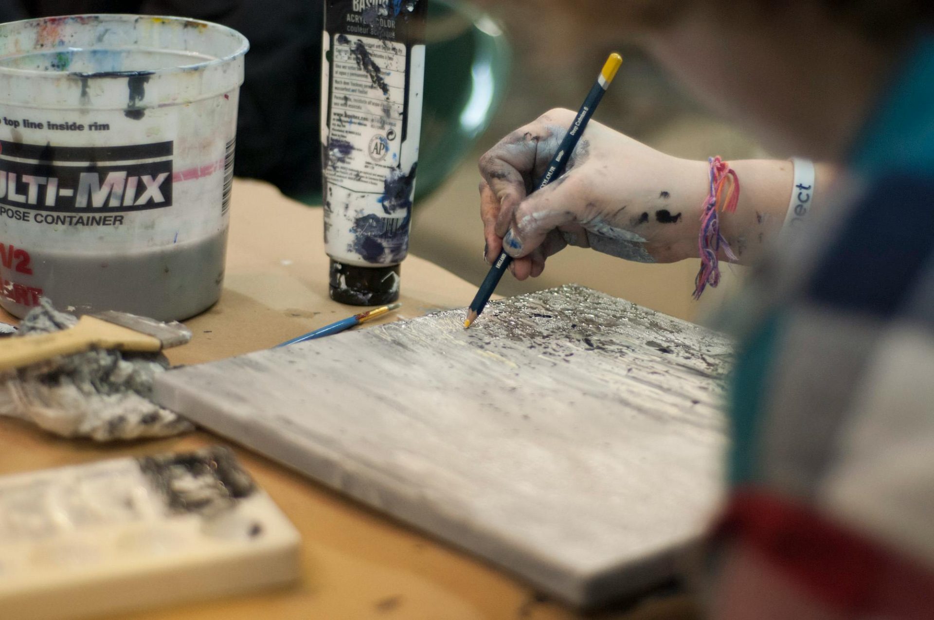 Close-up of an artist's hand painting a textured abstract piece. Creative process in studio.